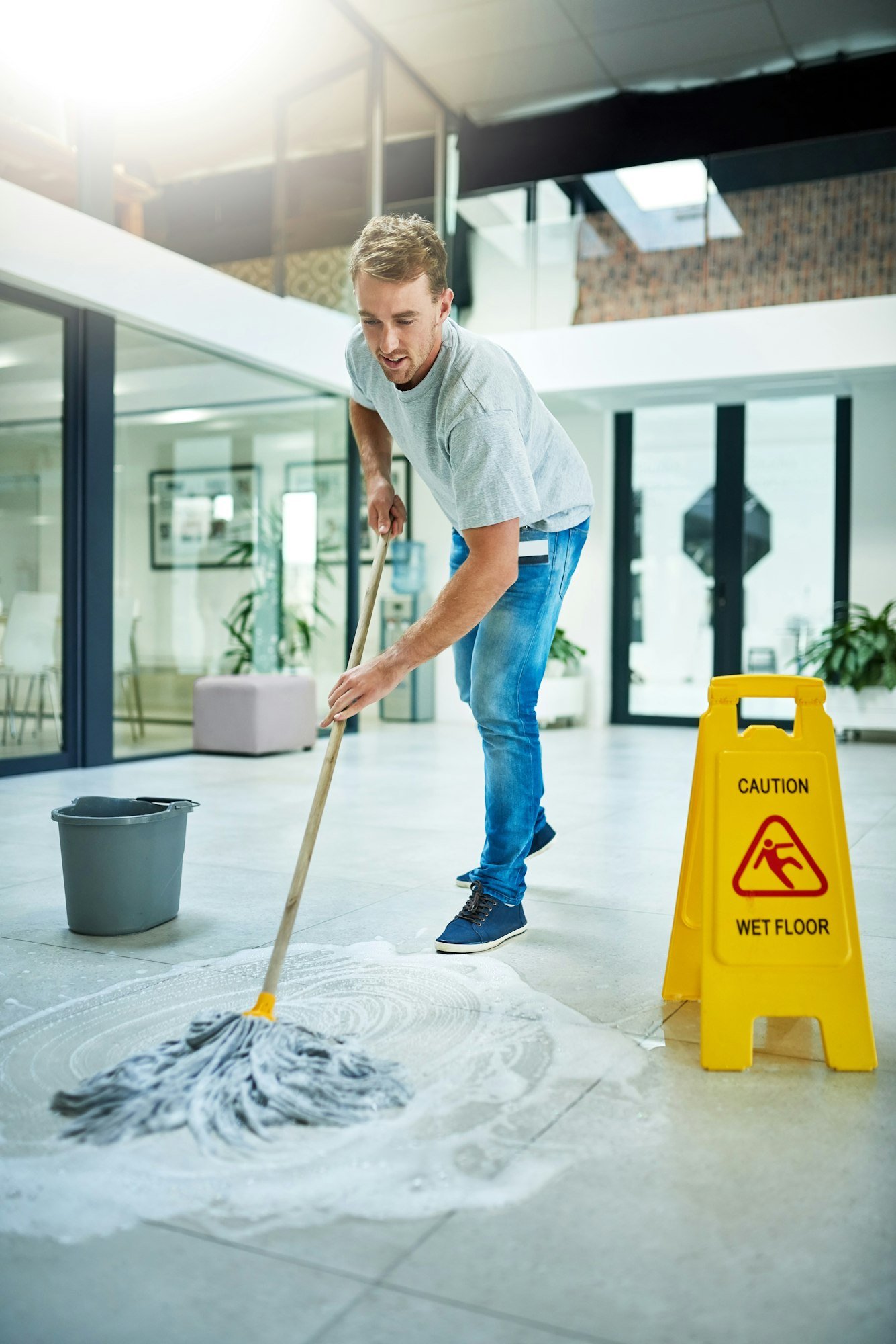 Giving it some elbow grease. Shot of a young man mopping the office floor.